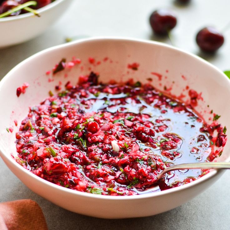 a bowl filled with cranberry sauce next to another bowl full of cherries