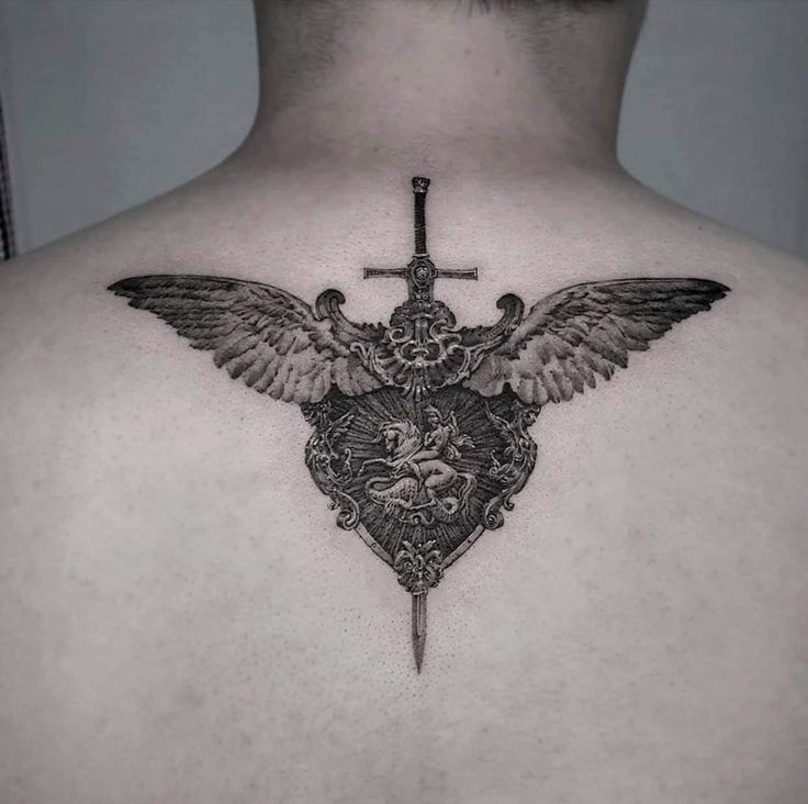 the back of a man's chest with a cross and wings on top of it