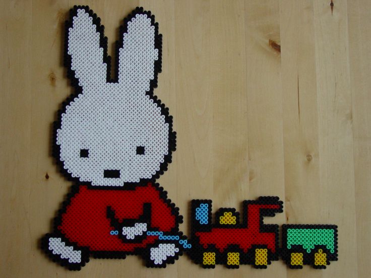 a cross stitch pattern of a white rabbit playing with a toy train on a wooden surface