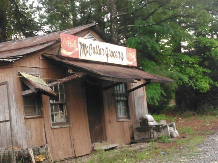 an old run down building sitting in the middle of a forest with a sign on it's roof