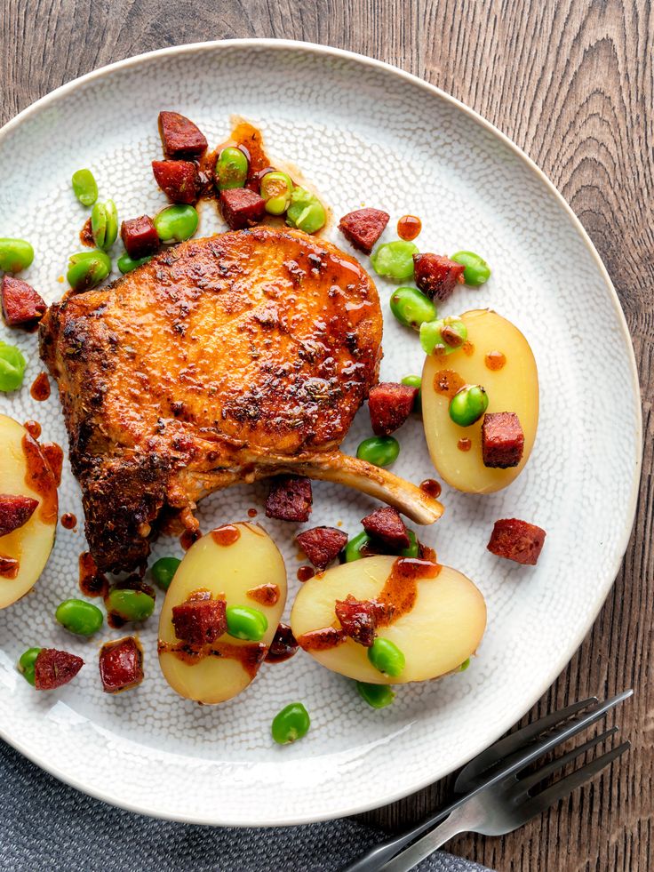 a white plate topped with meat and potatoes on top of a wooden table next to utensils