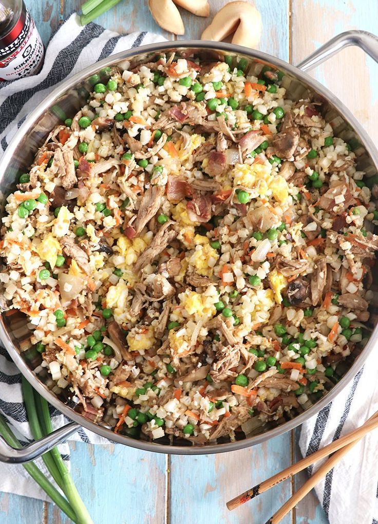 a pan filled with rice and vegetables on top of a blue wooden table next to chopsticks