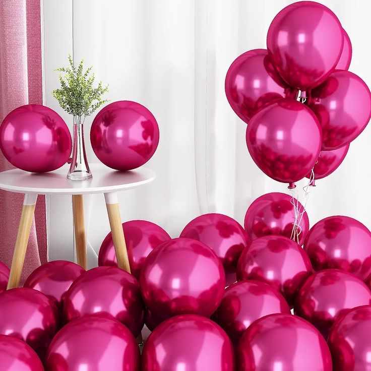 a bunch of pink balloons sitting on top of a table next to a white table