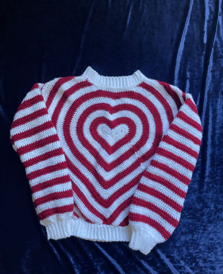 a red and white striped sweater with a heart on the chest, sitting on a blue velvet surface