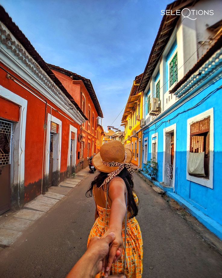 a woman in a yellow dress and straw hat walking down the street with her hand on another person's shoulder