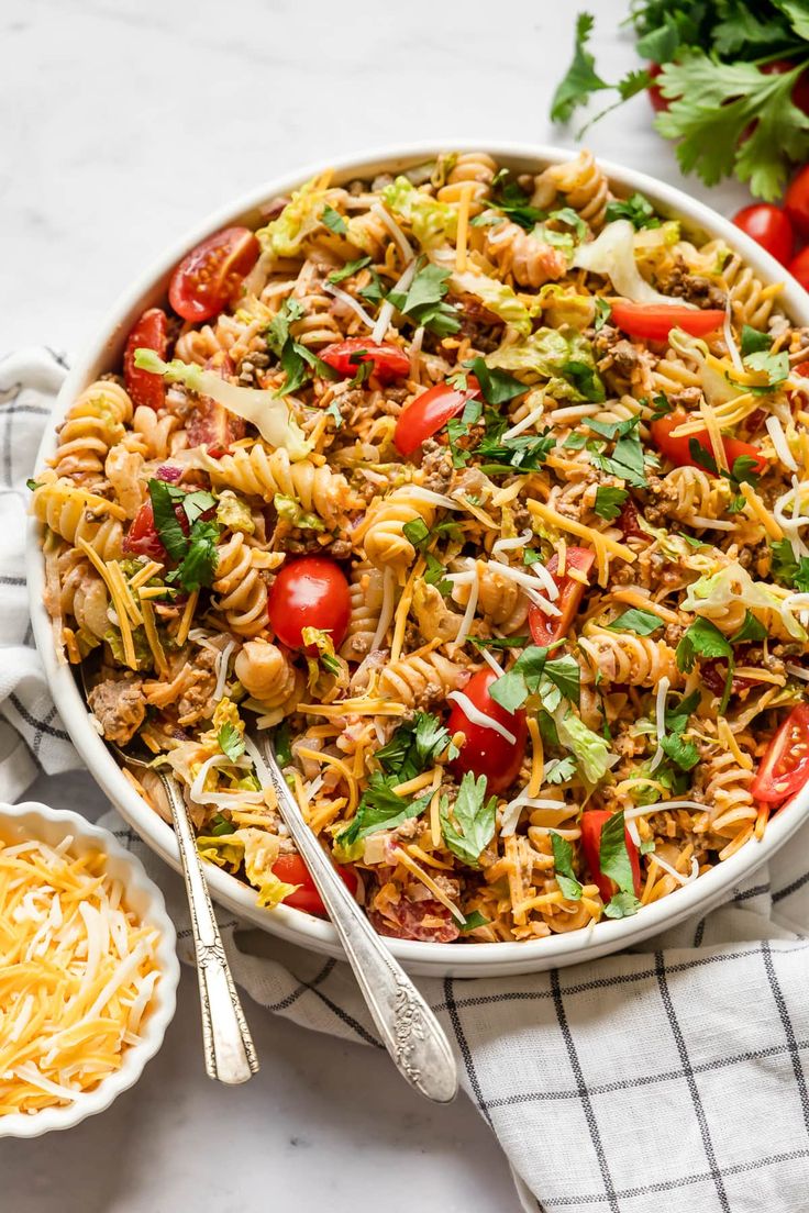 a large bowl filled with pasta salad next to two small bowls of cheese and tomatoes