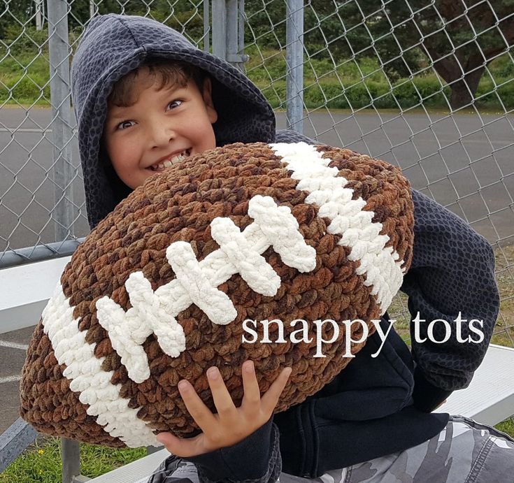 a young boy holding a crocheted football pillow