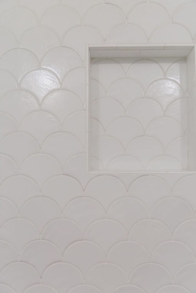 a white bathroom with a square window on the wall and fish scale pattern on the walls