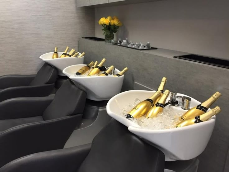 four white bowls filled with champagne bottles in a room next to a counter and yellow flowers