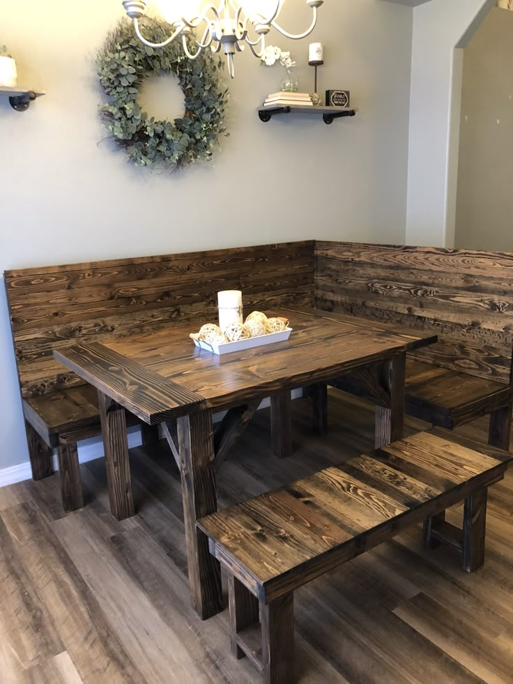 a wooden table and benches in a room with white walls, wood flooring and chandelier hanging from the ceiling