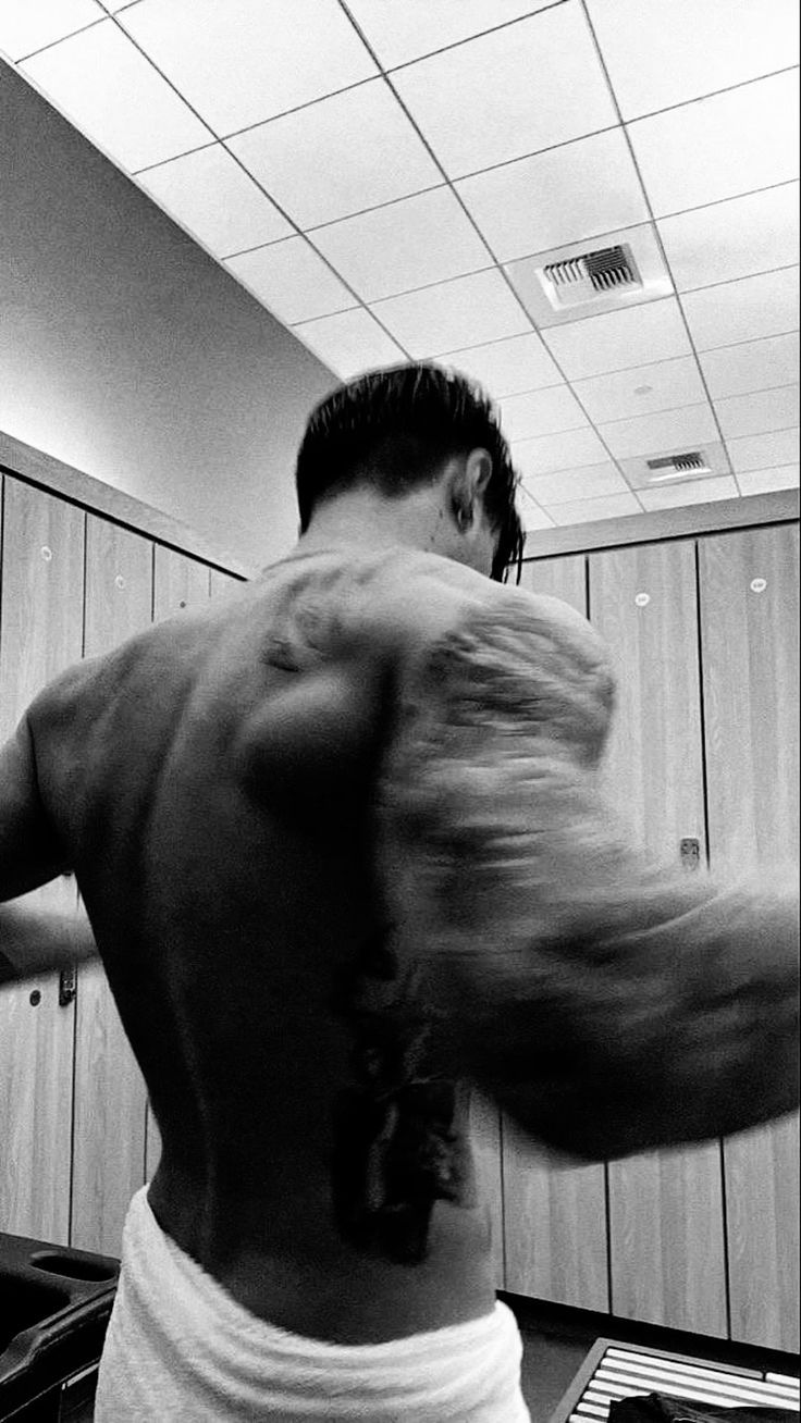 a man with no shirt on standing in front of a locker room door and holding his arm out