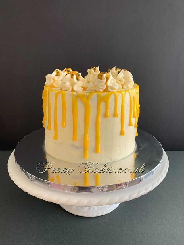 a cake with yellow icing and white frosting on a glass platter next to a gray wall