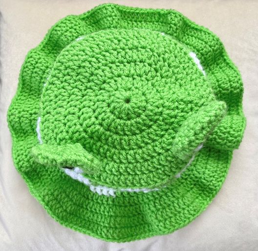 a green crocheted dish cover sitting on top of a white bed next to a pillow