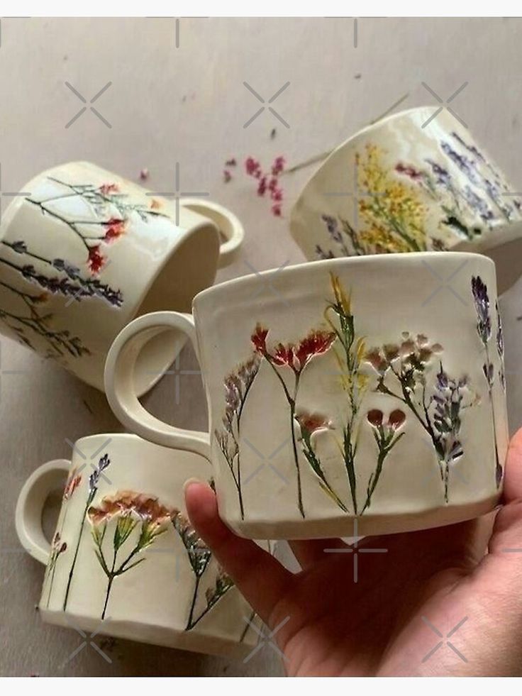 hand painted coffee cups and saucers with wildflowers on them are being held in front of the camera