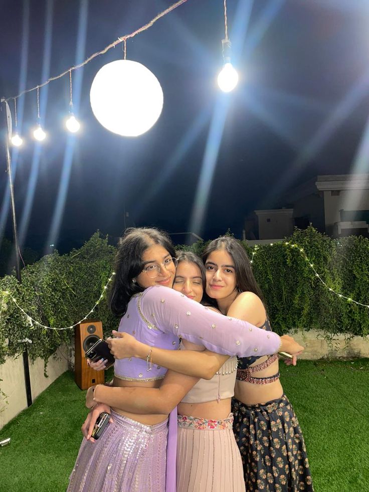 three young women standing next to each other on top of a lush green field at night