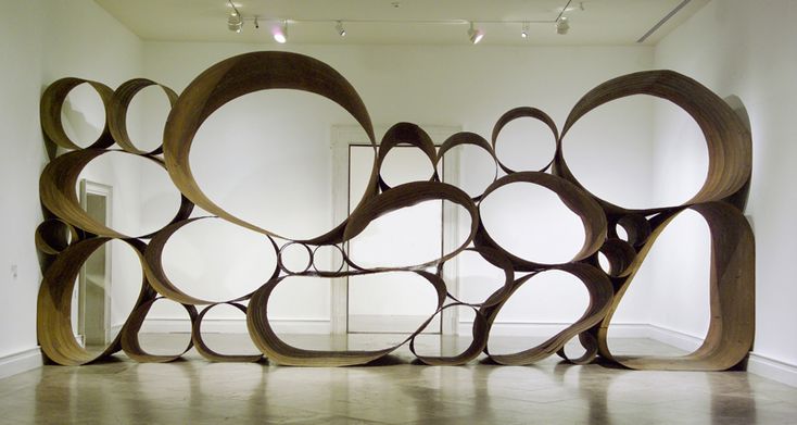 a sculpture made out of circles in an empty room with mirrors on the wall behind it