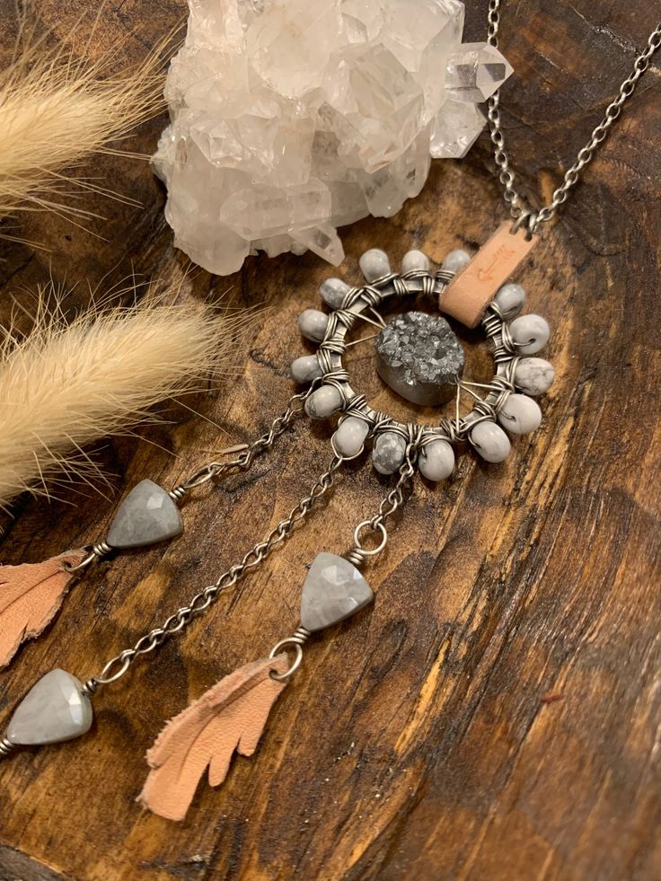 Dream Catcher Talisman Necklace // GreyChain length: 18"Dream Catcher Length: 5.5"Dream Catcher Width: 1.5"Wire wrapped Howlite surround a sterling circle with a silver colored druzy in the center. Dangling below are three triangle gray silverite facetted gemstones and handmade leather 'feathers'. This statement necklace is a homage to the Native American dream catcher. A talisman representing this beautiful concept of an artful handmade hoop with stones, feathers, string and wire that will catc Bohemian Silver Necklace With Raw Stone, Artisan Silver Necklace With Raw Stone, Silver Necklace With Raw Stone Round Pendant, Hand Wrapped Silver Necklaces For Festivals, Festival Hand Wrapped Silver Necklaces, Bohemian Sterling Silver Hand-wrapped Necklaces, Bohemian Sterling Silver Hand Wrapped Necklaces, Bohemian Silver Crystal Necklace With Round Pendant, Silver Hand Wrapped Round Pendant Jewelry