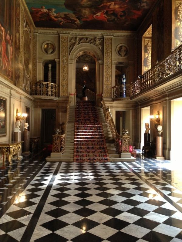 an elaborately decorated hallway with black and white checkered flooring, chandelier and staircase leading up to the second story