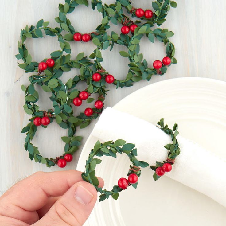 a hand holding a napkin over a plate with holly wreaths on it and red berries