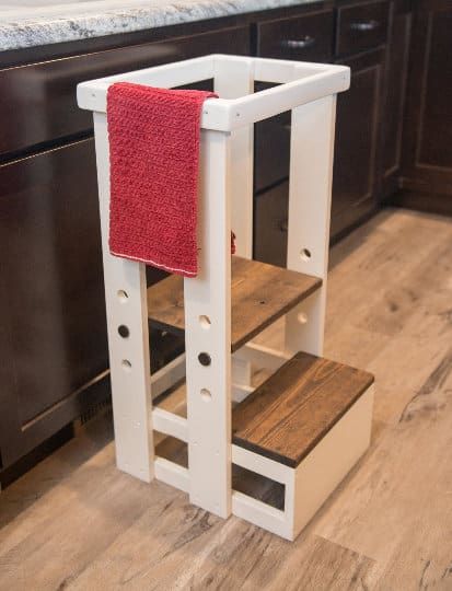 a wooden step stool with a red towel hanging on it's side in a kitchen