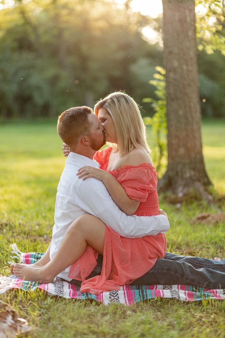 a man and woman kissing while sitting on a blanket