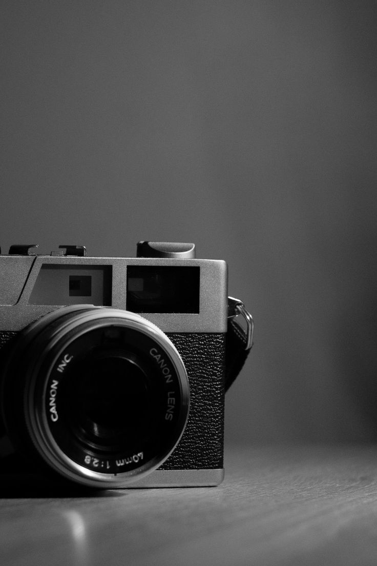 black and white photograph of an old camera on a wooden table in front of a wall