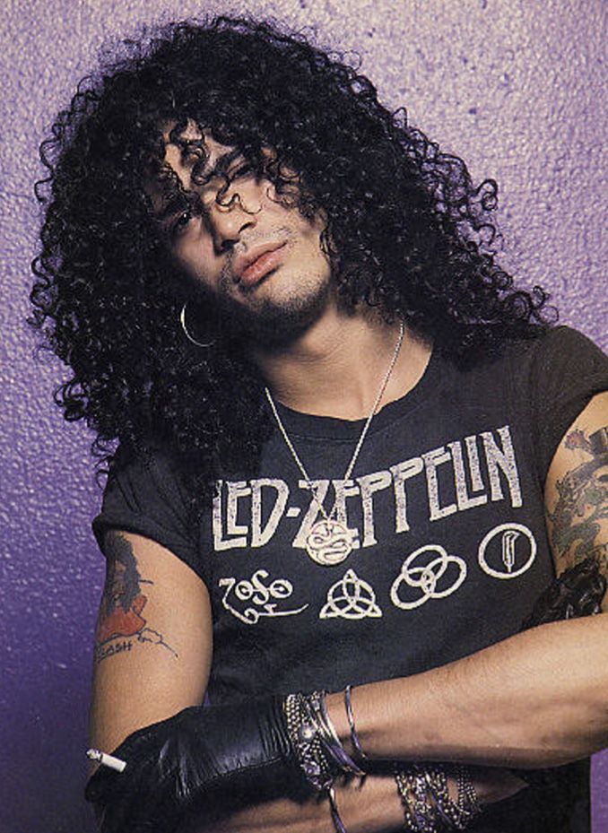 a black and white photo of a man with long curly hair wearing a t - shirt