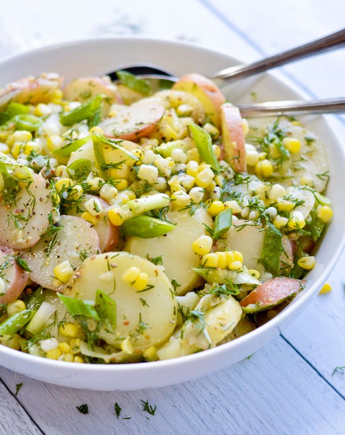 a white bowl filled with potatoes, corn and herbs