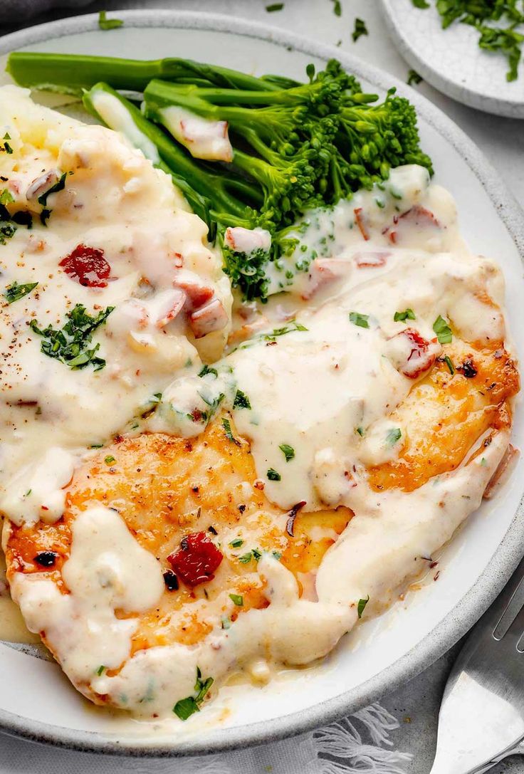 a white plate topped with chicken covered in gravy and broccoli spears