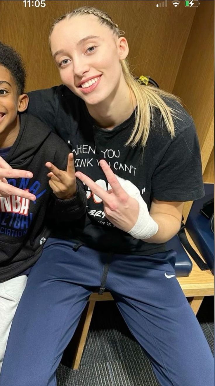 a woman sitting next to a boy in a locker room with his hands up and smiling at the camera