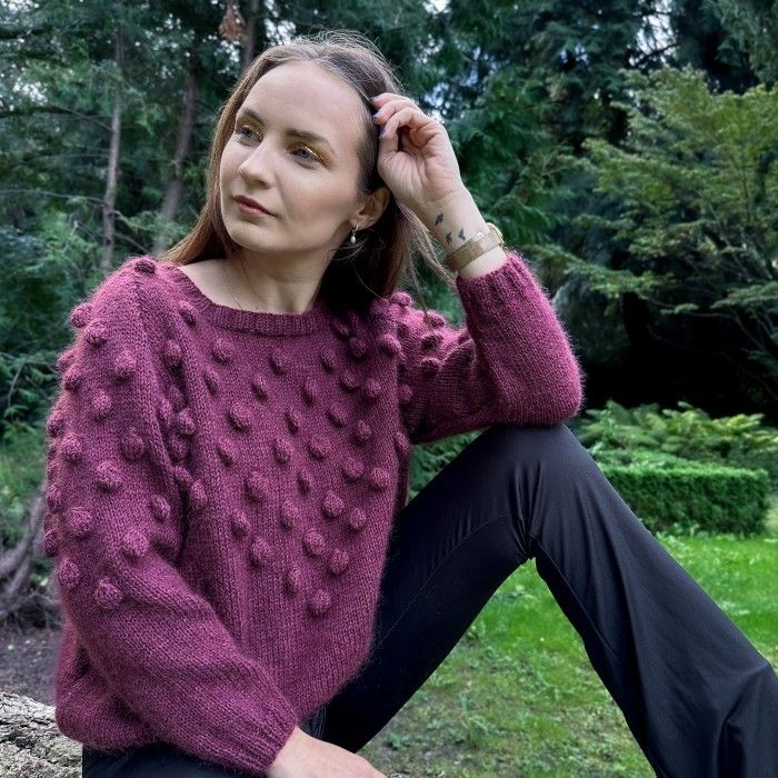 a woman sitting on the ground wearing a purple sweater and black pants with her hands in her hair