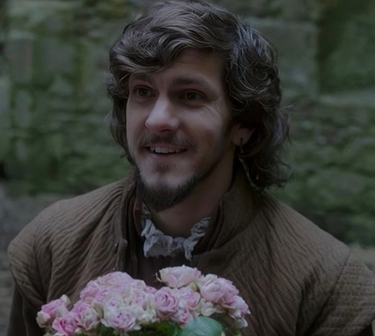 a man with long hair holding a bouquet of flowers in front of him and smiling at the camera