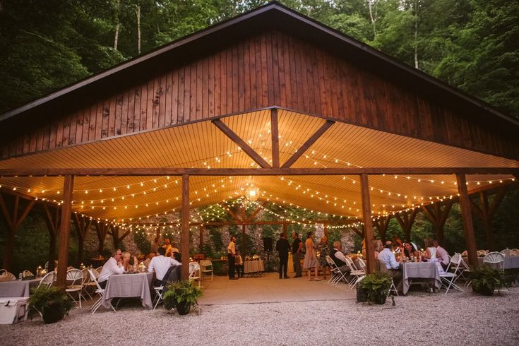 a group of people sitting at tables under a covered area with lights strung from the ceiling