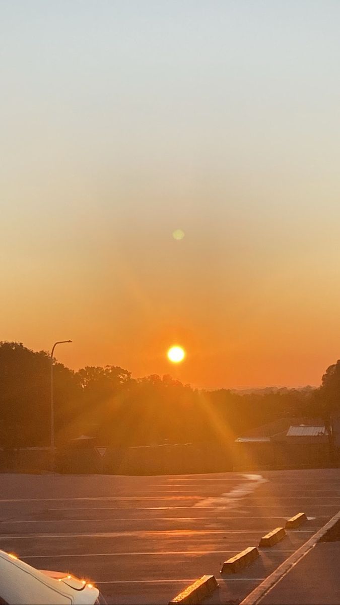 the sun is setting over an airport parking lot