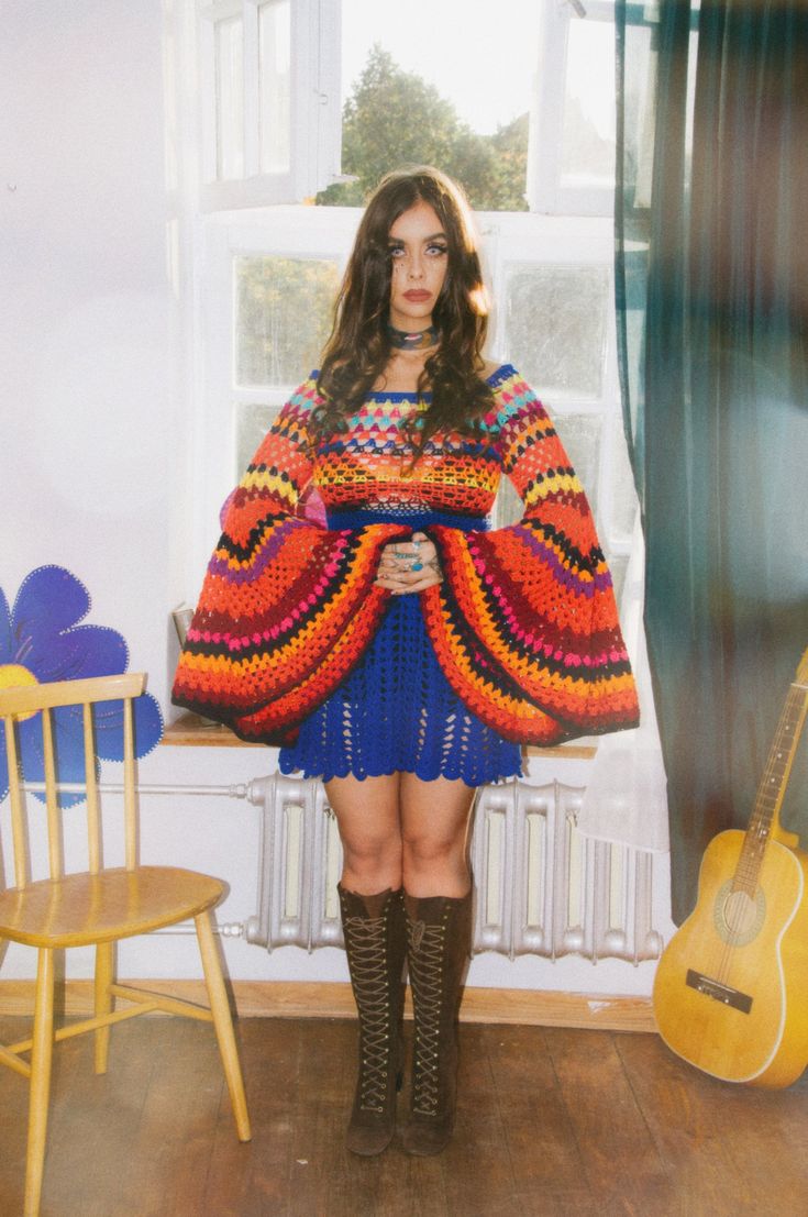 a woman standing in front of a window wearing a colorful dress and holding a guitar