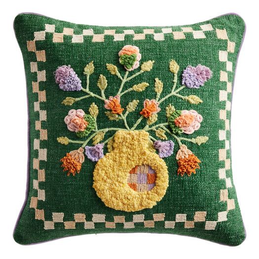 a green pillow with an embroidered flower arrangement on the front and side, along with a checkered border