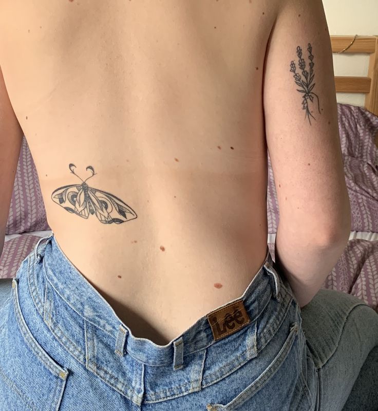 a person with a butterfly tattoo on their back, sitting on a bed and looking at the camera