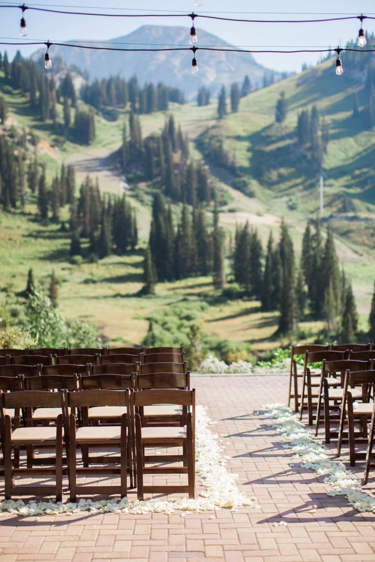 rows of wooden chairs set up in front of a scenic mountain backdrop with string lights