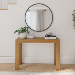 there is a mirror on the wall next to a wooden table with plants and books