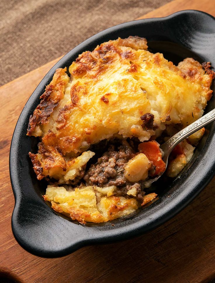 a skillet filled with food on top of a wooden cutting board next to a fork