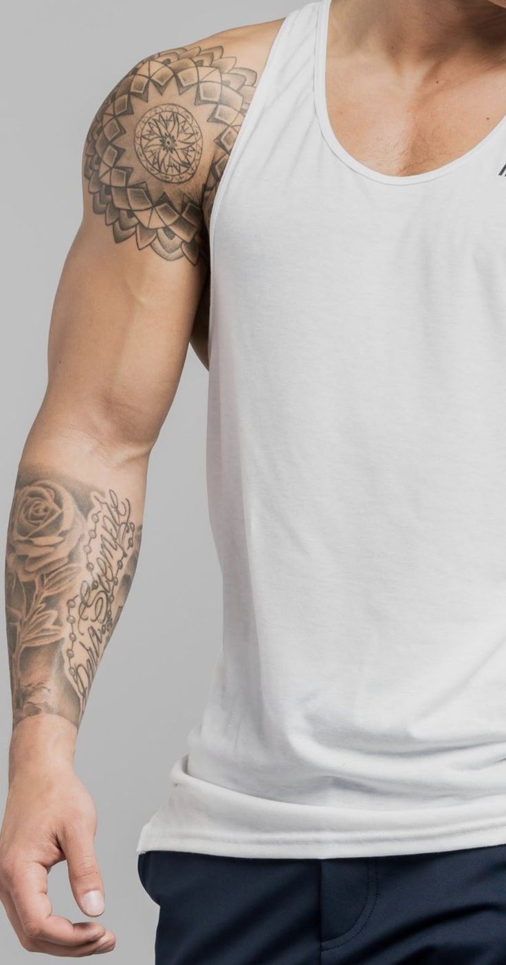 a man wearing a white tank top with tattoos on his arm