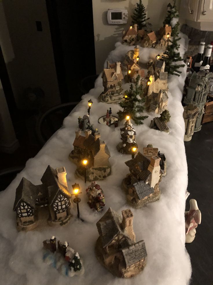 a table topped with lots of small christmas village figurines and lights on top of snow covered ground