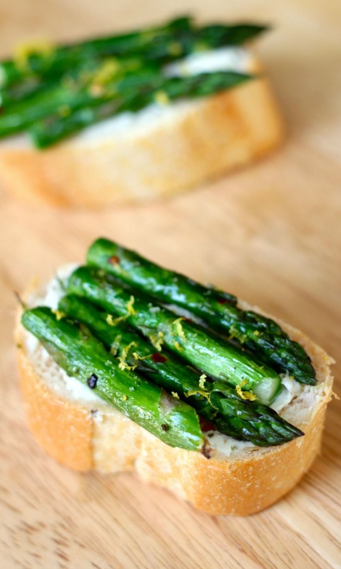 two pieces of bread with green asparagus on them sitting on a wooden table