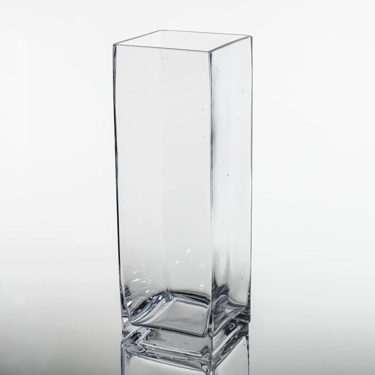 a tall clear glass vase sitting on top of a table next to a white wall