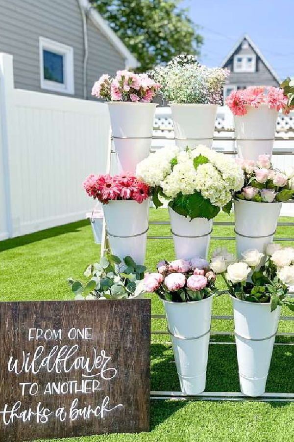 a bunch of flowers that are sitting in buckets on the grass next to a sign