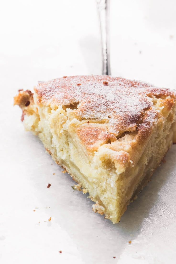 a piece of cake sitting on top of a white table next to a fork with powdered sugar on it