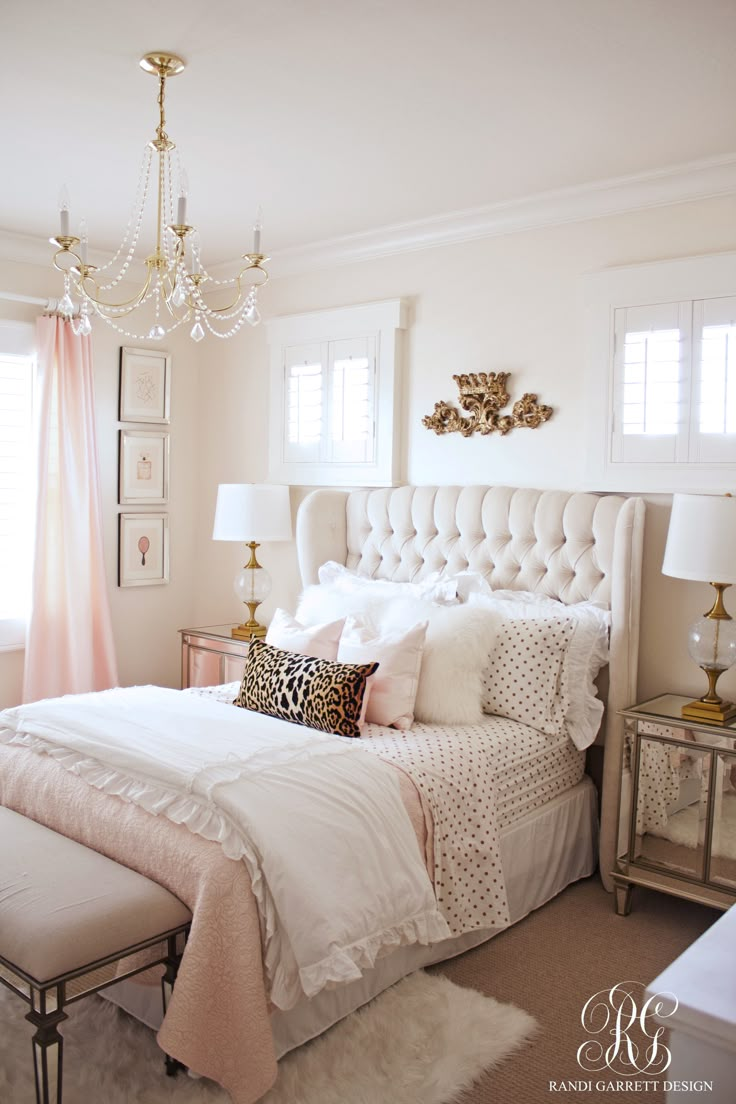 a bed with white sheets and pillows in a bedroom next to a chandelier