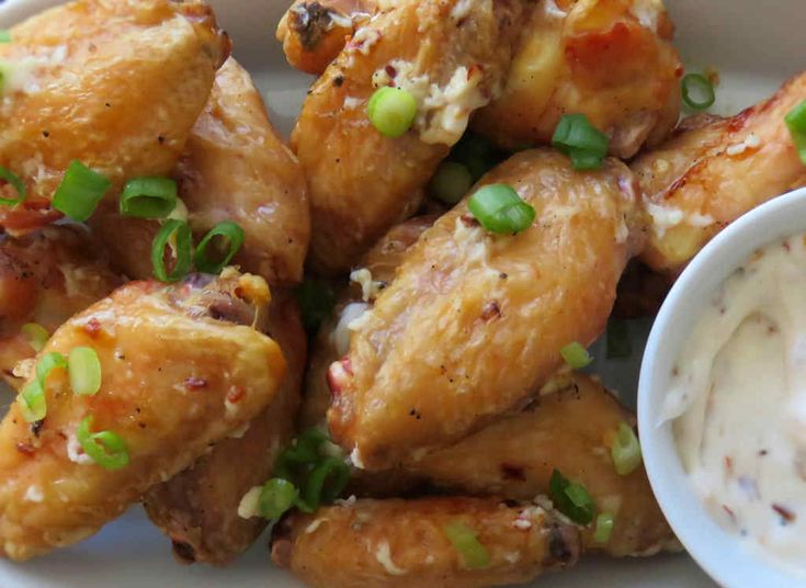 a white plate topped with chicken wings covered in ranch dressing