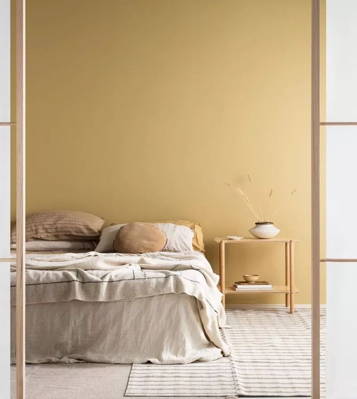 a bed sitting in a bedroom next to a wall with yellow paint on the walls