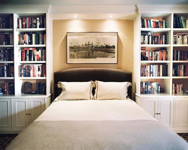 a bed with white sheets and pillows in front of bookshelves filled with books